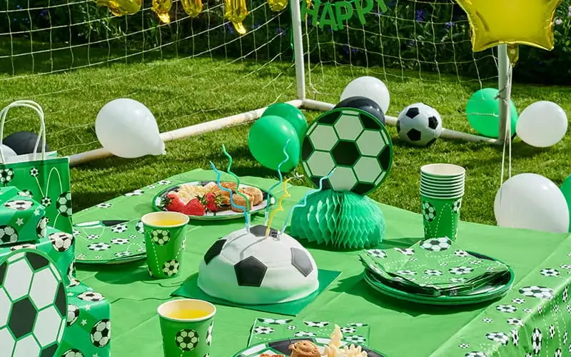 Football-themed birthday party table with a football-shaped cake, football-print tableware, balloons, gift bags, and a Happy Birthday balloon banner.